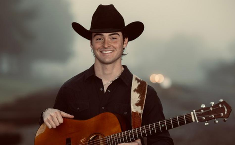 Presley Barker standing on train tracks holding a guitar in the fog.